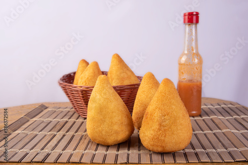 Brazilian Chicken Croquettes, coxinha, and glass of chili sauce over wooden surface, gray background, selective focus. photo