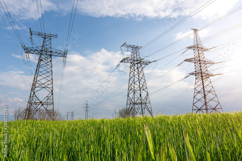 High voltage lines and power pylons and a green agricultural landscape on a sunny day.