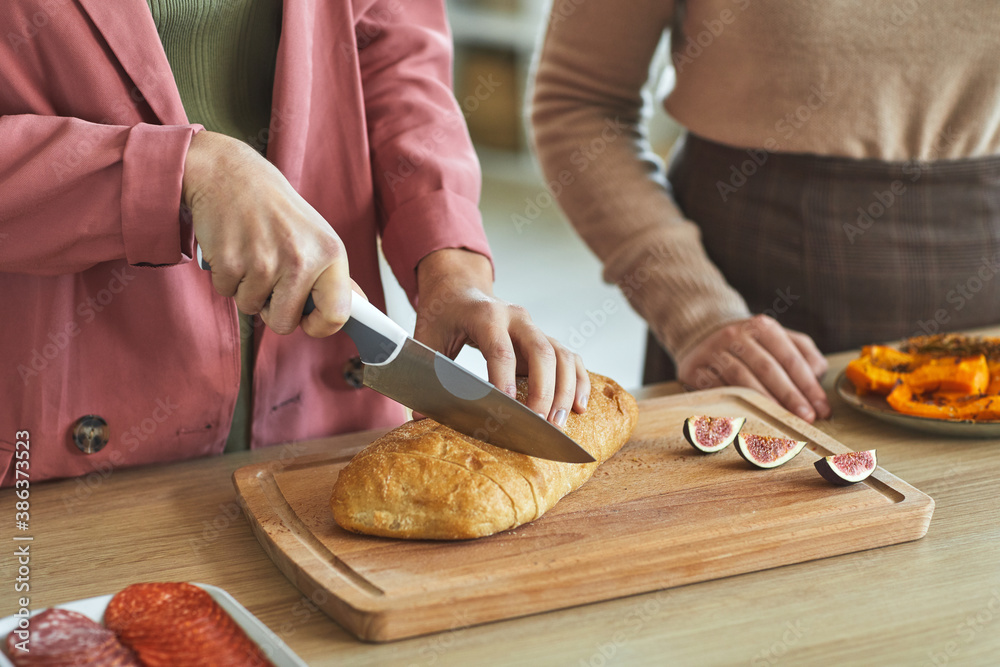 Close up of two unrecognizable women cutting fresh bread while cooking for dinner party, copy space Close up of two unrecognizable women cutting fresh bread while cooking for dinner party, copy space