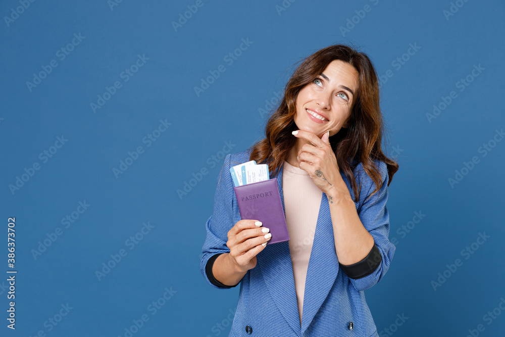 Pensive young traveler tourist woman in jacket hold passport tickets put hand prop up on chin isolated on blue background. Passenger traveling abroad on weekends getaway. Air flight journey concept. Pensive young traveler tourist woman in jacket hold passport tickets put hand prop up on chin isolated on blue background. Passenger traveling abroad on weekends getaway. Air flight journey concept.