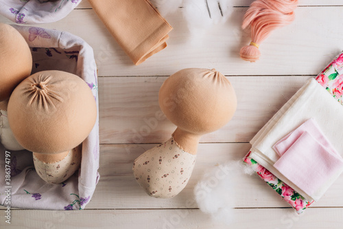 Textile doll in the sewing process with accessories and materials: fabric, thread, needle on white wooden background photo