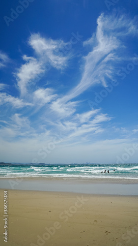 Windy day at the beach: featuring a blue sky with windswept clouds, people in the surf, and a sandy beach.