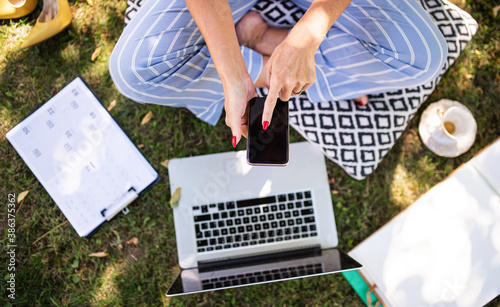 Unrecognizable woman working in home office outdoors in garden, using smartphone and laptop. photo