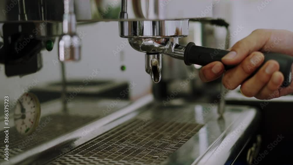 The barista holds the porta-filter pressed into the machine. The person serving the coffee brings a cup to support the dripping coffee. Part of the coffee making process