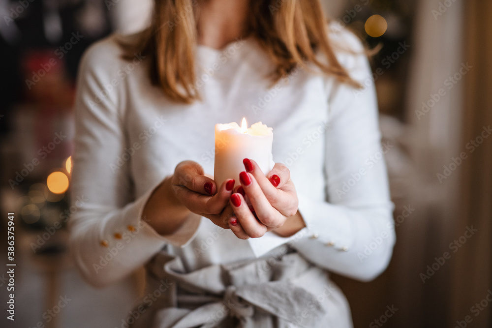 Unrecognizable young woman indoors at home at Christmas, holding candle.