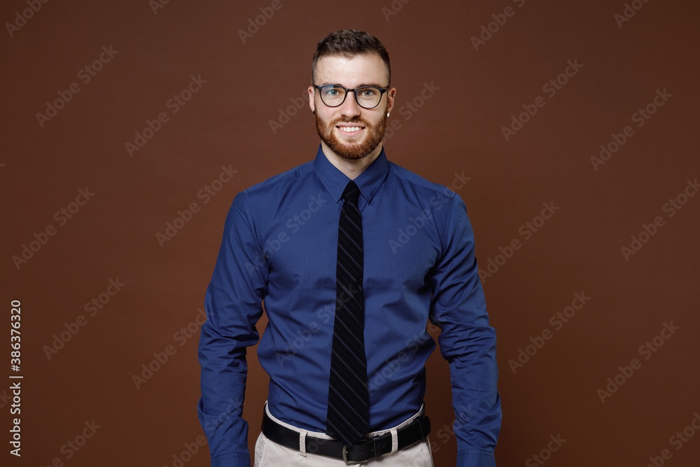Smiling successful handsome bearded young business man in blue shirt tie eyeglasses looking camera isolated on brown colour background studio portrait. Achievement career wealth business concept. - obrazy, fototapety, plakaty 