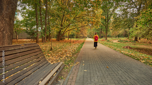 lonely suluet woman in yellow jacket on deserted alley in autumn city park photo