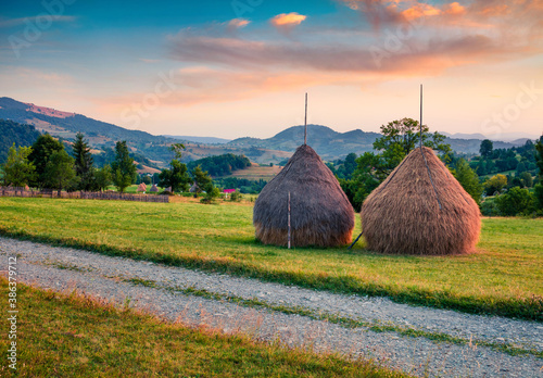 Fantastic sunrise on Rogojel village. Two haystacks on the mountain lawn. Nice summer scene of Cluj County, Romania, Europe. Beauty of countryside concept background. photo