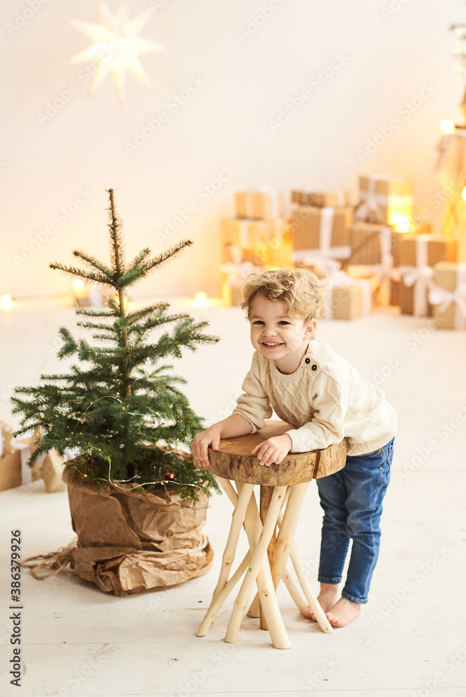Handsome curly little boy decorated a Christmas tree in a white room