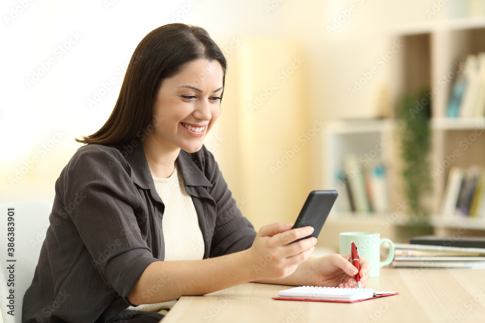 Happy woman writing in agenda and checking phone Happy woman writing in agenda and checking phone
