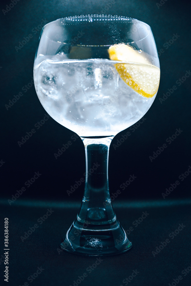 Gin and tonic cocktail with a lemon slice on black background. Alcohol, drink, ice, shallow depth of field, focus.