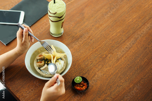 Top view of woman hands eating Indonesian Famous Foodstreet Bakso / Meatballs served with noodles, rice noodles and fried  dumpling crispy or pangsit with avocado juice for drink photo