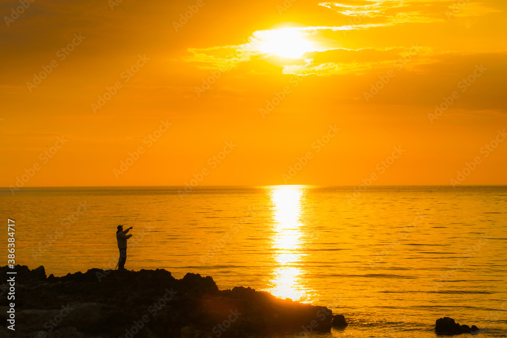 silhouette of a fisherman fishing by the sea at sunset
