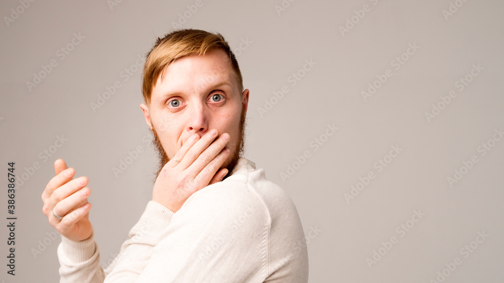 Portrait of young man covering his mouth with one hand, isolated on gray background Portrait of young man covering his mouth with one hand, isolated on gray background