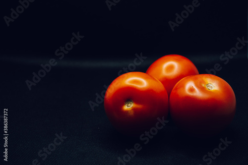 A trio of tomatoes on black background. Shallow focus, blur, red, 3, food prep, contrast, dark, lighting.