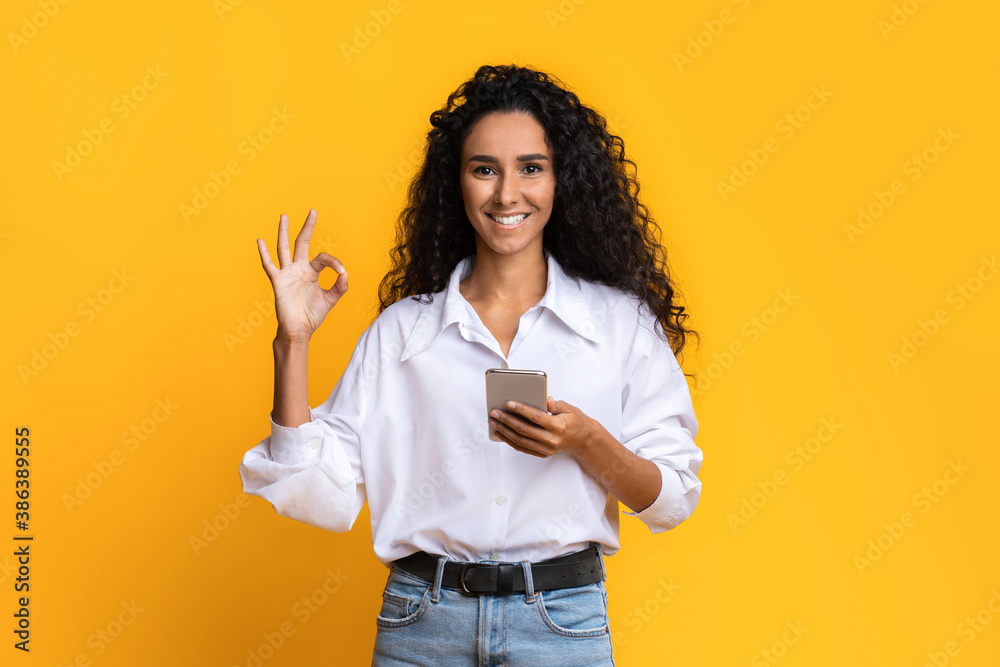 Great Mobile Offer. Smiling young woman holding smartphone and showing ok gesture Great Mobile Offer. Smiling young woman holding smartphone and showing ok gesture