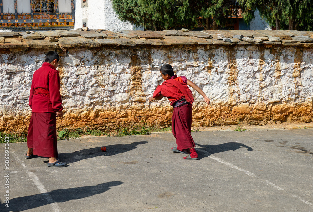 Bhutan, young monks having fun and playing football in front of their monastery.
