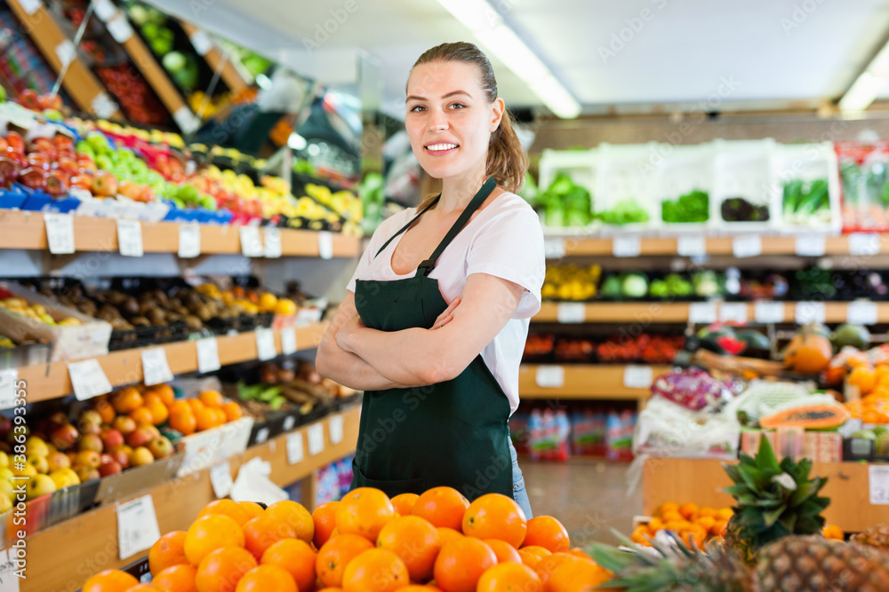 Happy cheerful woman in apron working holding fresh oranges in hands on the supermarket.