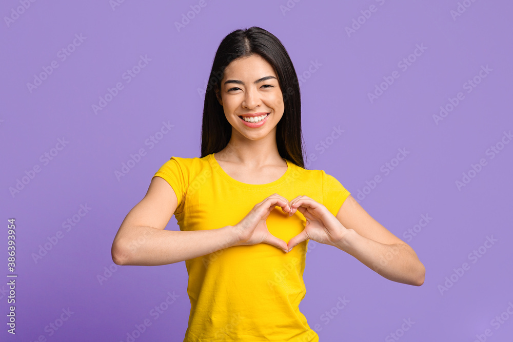 Friendly asian woman shaping hands like heart, making love gesture near chest Friendly asian woman shaping hands like heart, making love gesture near chest