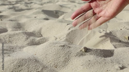 A woman's hand pouring sand through her fingers on a sandy beach