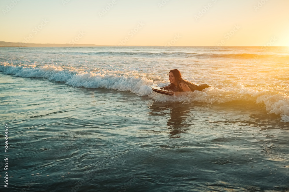 Woman riding a bodyboard at sunset, Moana Beach, South Australia