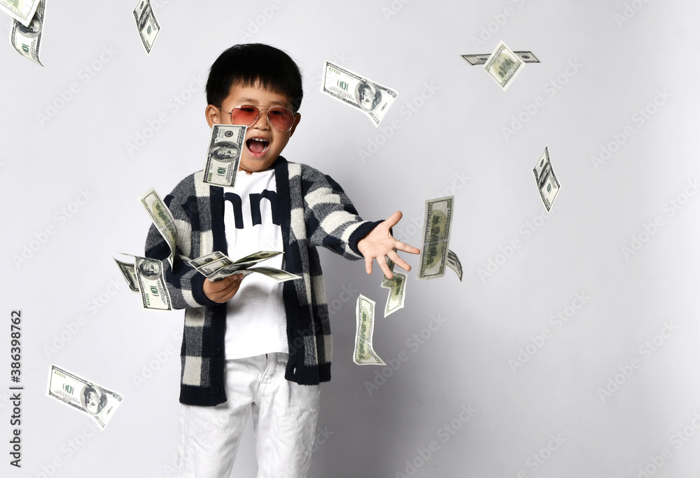 Happy shouting self-confident asian rich kid boy millionaire standing with bunch of moneys throwing money dollars cash
