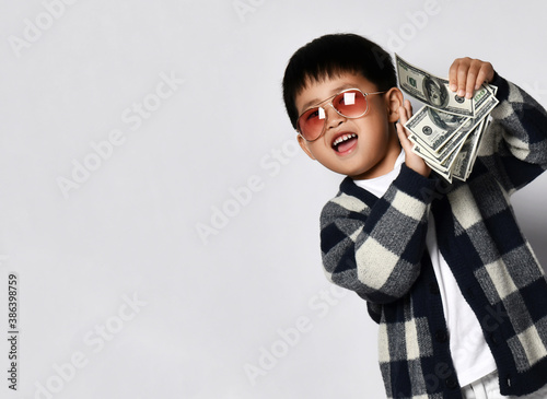 Happy smiling asian rich kid boy millionaire in modern sunglasses standing counting dollars cash bunch of money. Lucky winner photo