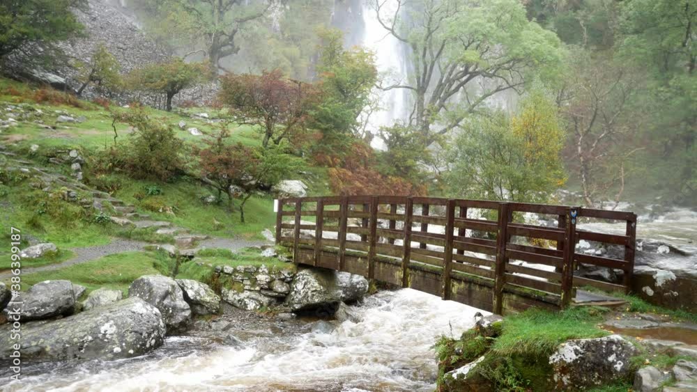 Idyllic wooden bridge over valley scenic mountain waterfall cascading into powerful zen flowing river Idyllic wooden bridge over valley scenic mountain waterfall cascading into powerful zen flowing river