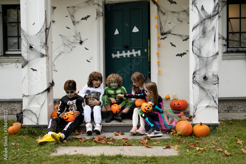 Group of trick-or-treating kids talking and sharing candies on a porch of a house during Halloween