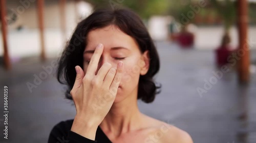 Woman practicing yoga exercise sitting in Sukhasana pose, performing nostril breathing technique outdoors