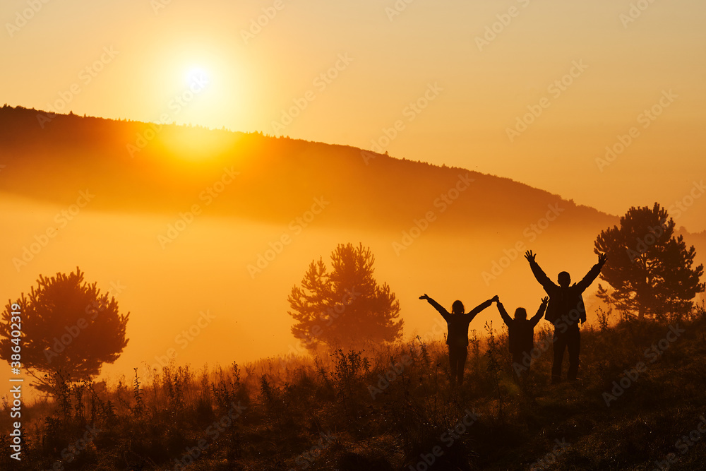 Beautiful fog in the morning. Silhouettes of three people - dad and two children against a beautiful golden sunrise. Hills in the Beskids, Poland.