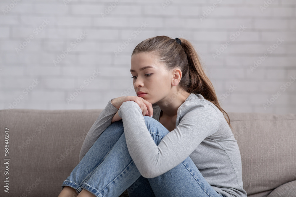 Young woman with depression sitting alone on sofa at home Young woman with depression sitting alone on sofa at home