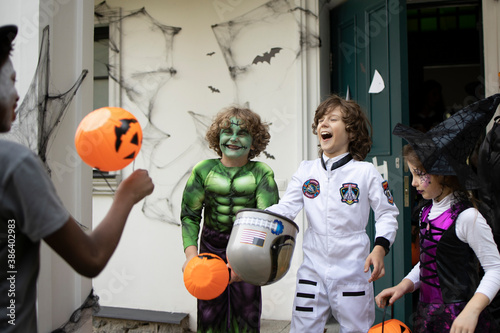 Group of trick-or-treating kids in face masks laughing on a porch of a house during Halloween