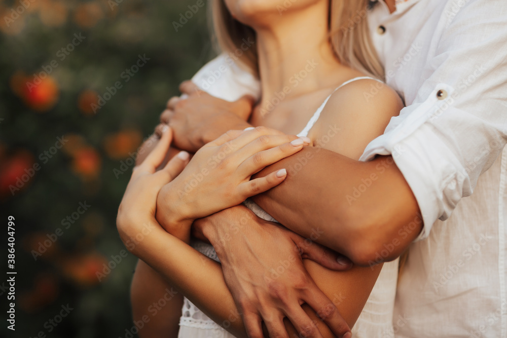 Cropped shot of a guy in a shirt hugs a girl in a white dress. Close-up hands together. Sensual shot.
