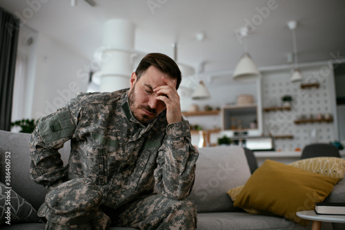 Depressed soldier sitting on sofa in living room. Young marine having PTSD.