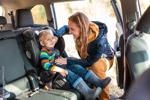 Mother fastening safety belt for her baby boy in his car seat.