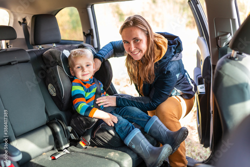 Mother fastening safety belt for her baby boy in his car seat.