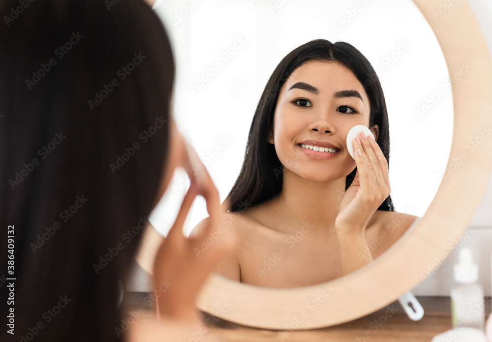 Smiling asian woman cleaning her face, using cotton pads Smiling asian woman cleaning her face, using cotton pads