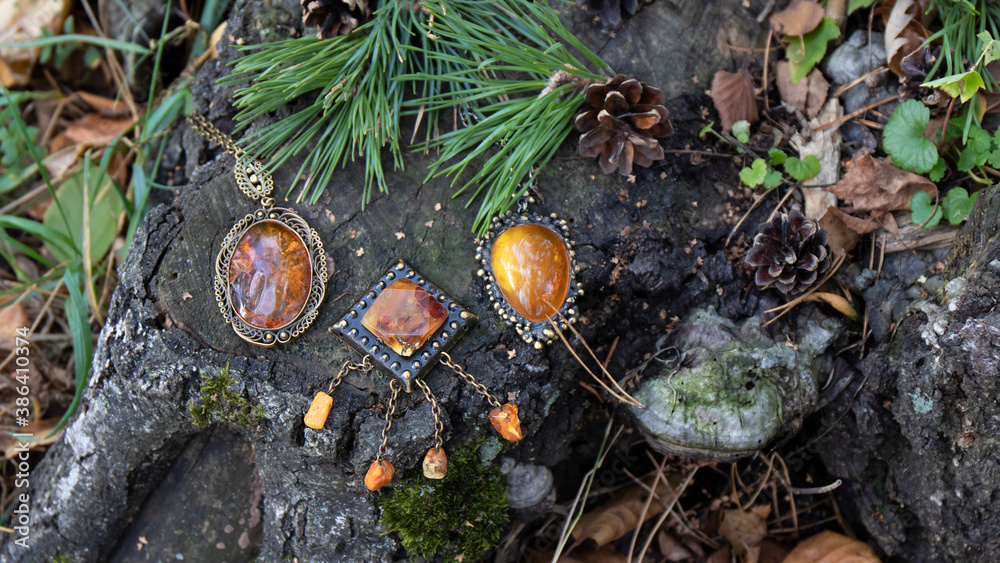 Obraz premium Sparkling vintage Baltic amber brooch and pendants lie among pine branches, cones and leaves on the aged tree stump in the forest. Amber is associated with love, healing, power, luck, strength, beaut