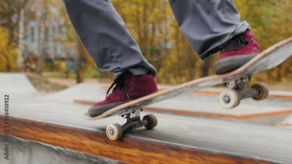 Skater practicing in the autumn concrete skate park, making tricks and rides in ramp. Skateboarder making tricks, manual balance, boardslide and stalls, professional extreme sport