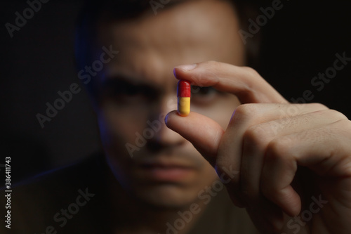 A man with a stern look in a dark room holds a tablet in a capsule in a dark room with a blue light