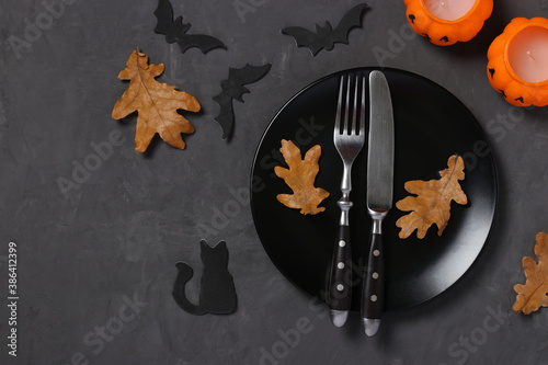 Halloween table setting is decorated with pumpkin shaped candles, bats and horror party decor on black table. Space for text.