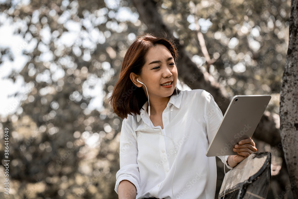 Portrait of a smiling young business woman using tablet for watching movies and listening music in the park with earphones. Changing workplace to create creative ideas and new ideas. Portrait of a smiling young business woman using tablet for watching movies and listening music in the park with earphones. Changing workplace to create creative ideas and new ideas.