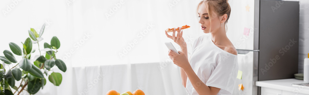 website header of young woman chatting on smartphone while holding pizza in kitchen website header of young woman chatting on smartphone while holding pizza in kitchen