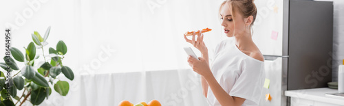 website header of young woman chatting on smartphone while holding pizza in kitchen