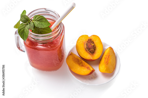 Watermelon cocktail in a jar with mint leaves, nectarine on a saucer and a cocktail straw on a white background.