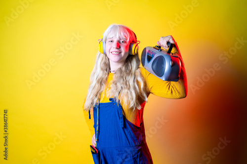 Young beautiful caucasian woman dancing indoor on yellow background holding vintage stereo - Isolated diverse female clubbing holding vintage radio