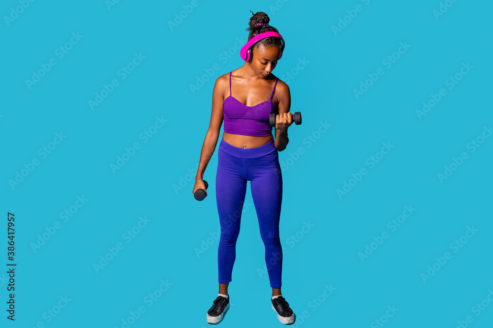 Fit young black woman weight lifting on blue background listening music - Isolated diverse black female workout with weights wearing headphones Fit young black woman weight lifting on blue background listening music - Isolated diverse black female workout with weights wearing headphones