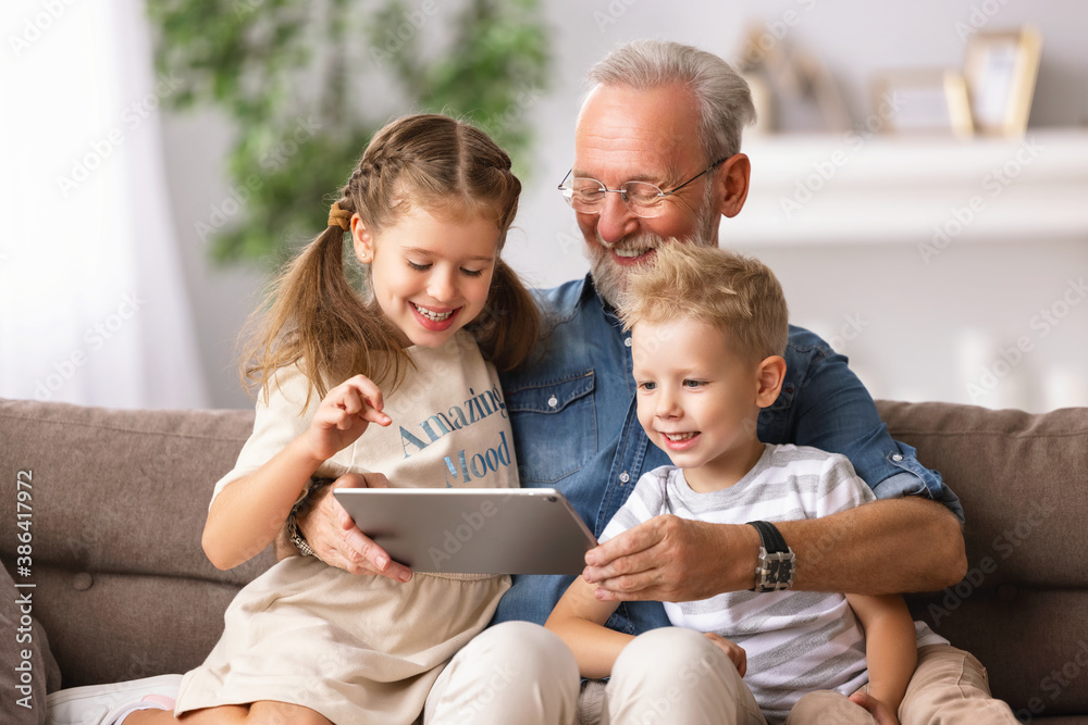 Grandfather and grandchildren using tablet on sofa.