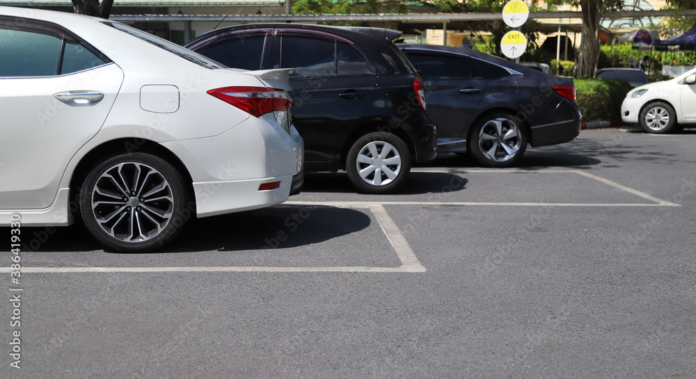 Closeup of rear side of white car with  other cars parking in outdoor parking area in bright sunny day. 
